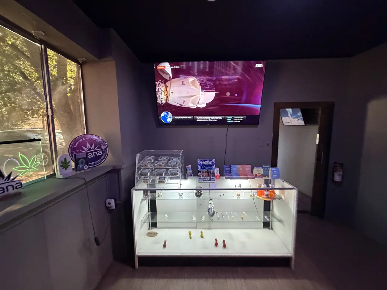A lit glass case with glass pieces and accessories, under a big screen