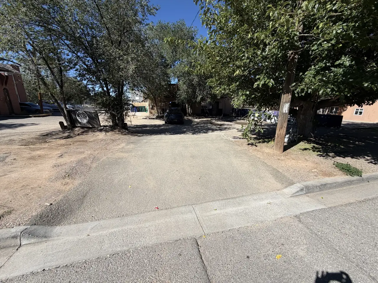 The curb cut off Luana St into the Deep Sky lot, with the Deep Sky sign on the left and the big tree on the right